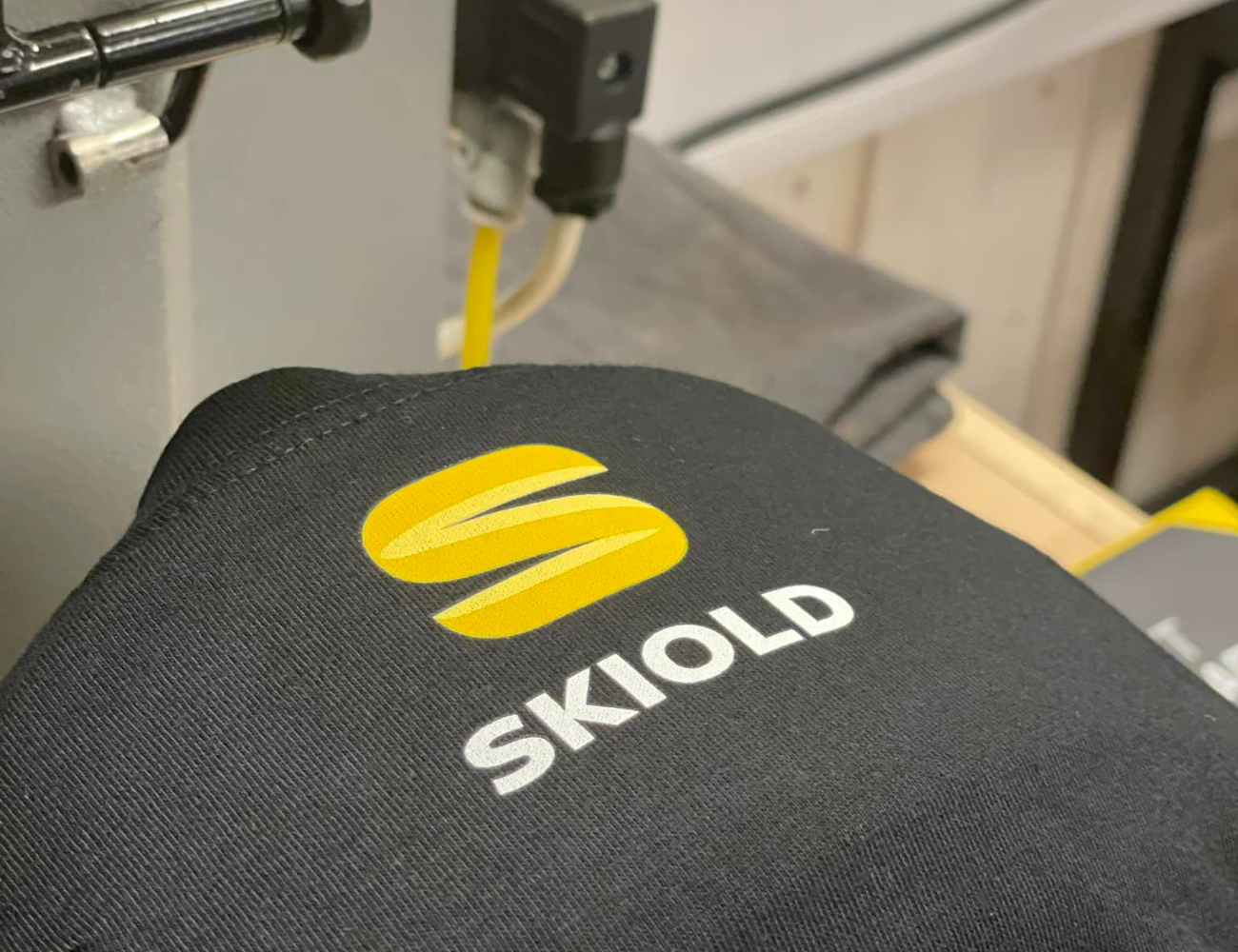 arbetskläder Bild på en svart tröja med gul logotyp och vit text "SKIOLD".